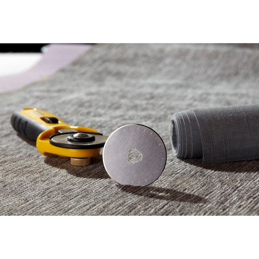 STANLEY STHT0-11942 rotary fabric cutter on grey textile surface, close-up with spare circular blade.