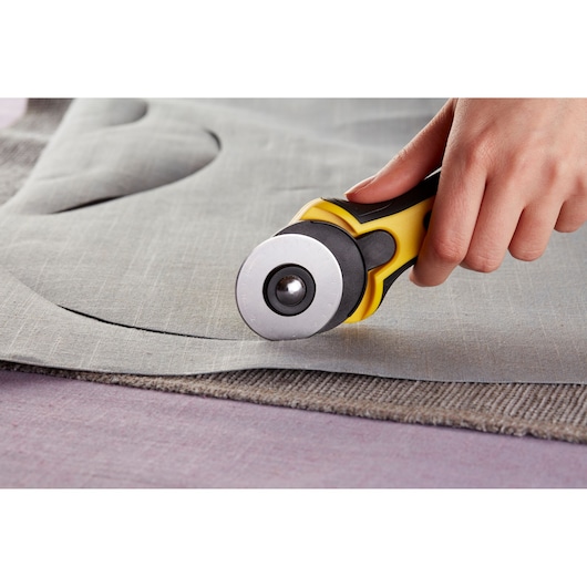 Photo of STANLEY STHT0-11942 rotary cutter cutting grey fabric, close-up view of hand using the tool.