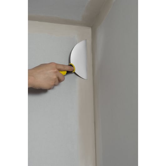 Hand using STANLEY STHT0-26088 putty knife with yellow handle to smooth wall corner.