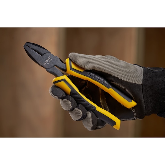 STANLEY STHT0-74367 combination pliers with yellow and black handles held by gloved hand.