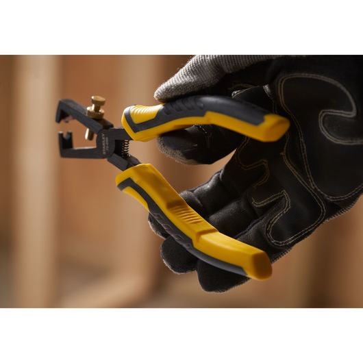 STANLEY STHT0-75068 wire stripper pliers with yellow and black handles held by a gloved hand, close-up.