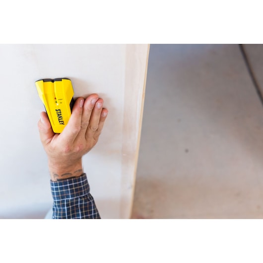 STANLEY STHT0-77050 stud finder held against a white wall by a hand.