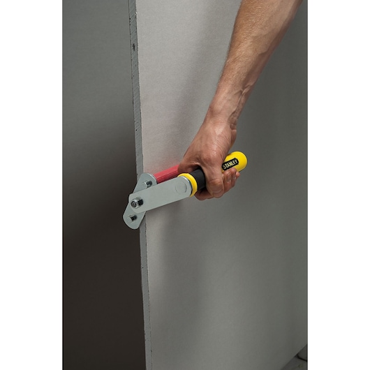 STANLEY STHT1-05868 drywall rasp with yellow handle trimming plasterboard edge, side angle photo.