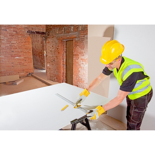 STANLEY STHT1-05933 utility knife used by worker in safety gear, cutting plasterboard on construction site.