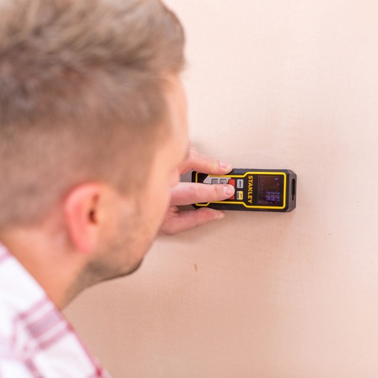 STANLEY STHT1-77138 laser distance measurer in use against a wall, close-up view.
