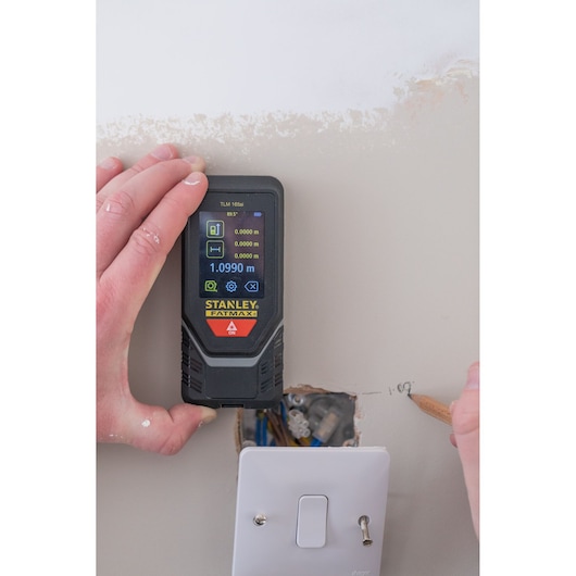 Photo of STANLEY STHT1-77142 laser distance measurer held against wall above electrical switch.