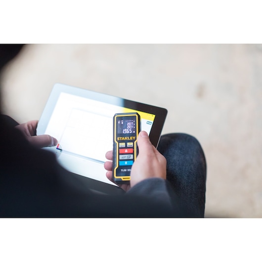 STANLEY STHT1-77343 laser distance measurer held in hand near tablet, close-up photo.