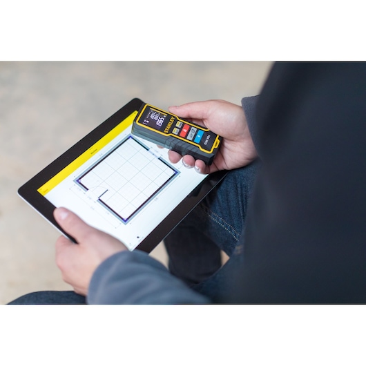STANLEY STHT1-77343 laser distance measurer next to tablet with floor plan, handheld, photography.