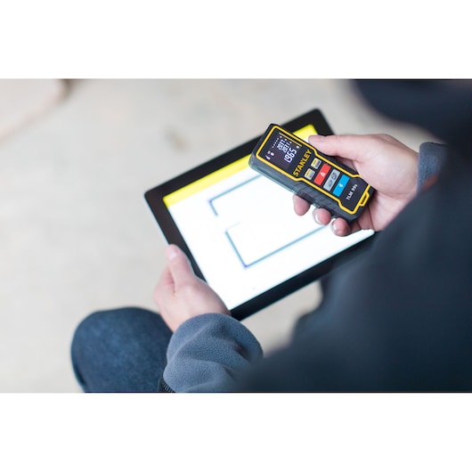 Photo of STANLEY STHT1-77343 laser distance measurer held above a tablet with floor plan.