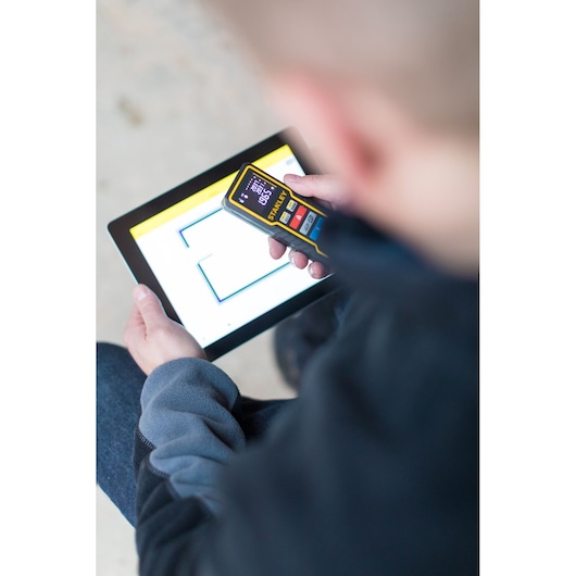 STANLEY STHT1-77343 laser distance measurer held above a tablet with a floor plan, top view.