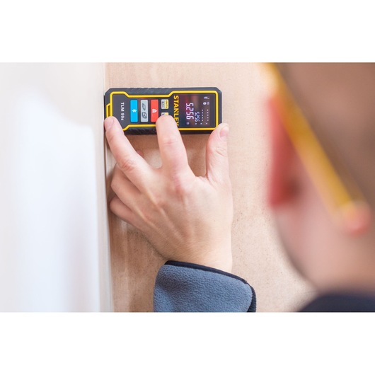 Photo of STANLEY STHT1-77343 laser distance measurer in use against a wall, held by a person's hand.