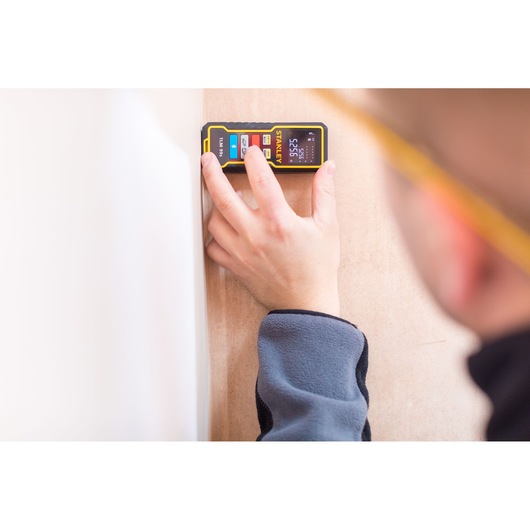 STANLEY STHT1-77343 laser distance measurer held against a wall, close-up of device and hand