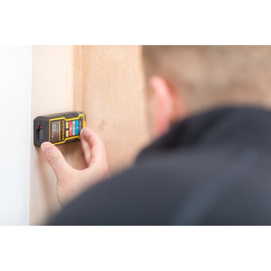 STANLEY STHT1-77343 laser distance measurer in use, person holding device against wall.