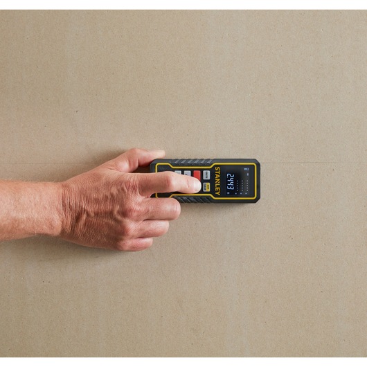 STANLEY STHT1-77343 digital laser distance measurer shown in use, hand pressing button against a wall, top view.