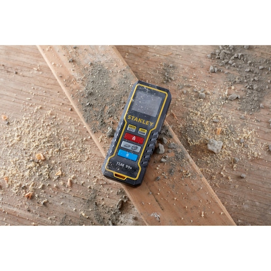 STANLEY STHT1-77343 laser distance measurer on wood plank, surrounded by dust and debris.