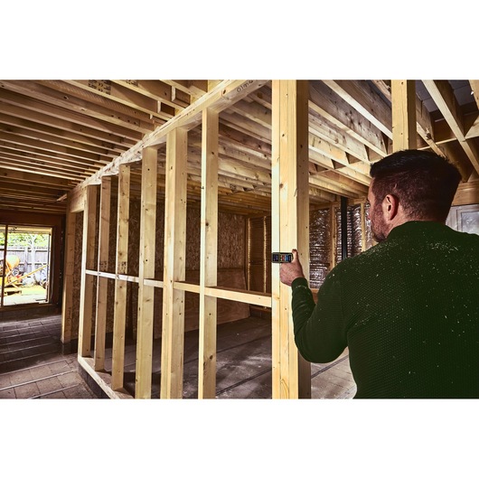 STANLEY STHT1-77343 laser distance measurer used on wooden framing, construction site scene.
