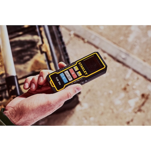 Photo of STANLEY STHT1-77343 laser distance measurer held in hand, black and yellow body with control buttons visible.