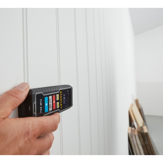 Photo of STANLEY STHT1-77361 laser distance measurer held against a white panel wall, close-up view.