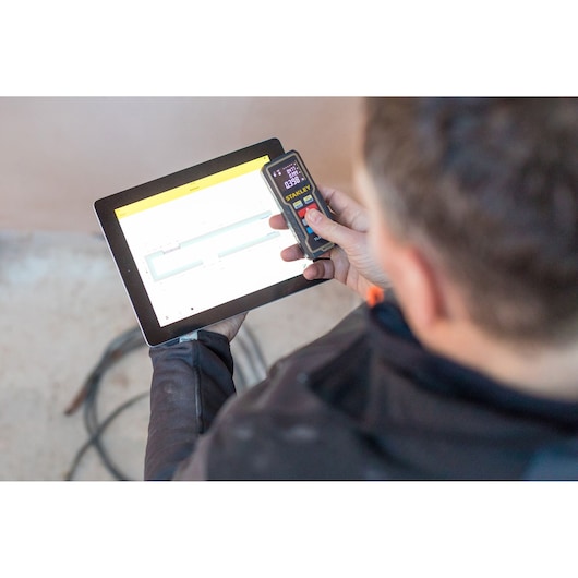 STANLEY STHT1-77361 laser distance meter shown in use with a tablet, photography category, angled handheld view.