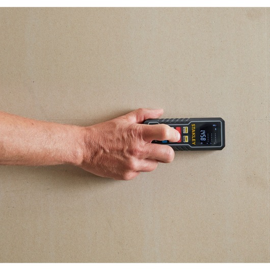 STANLEY STHT1-77361 digital laser distance measurer in hand, measuring on a wall, top view.