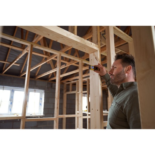 STANLEY STHT1-77409 laser distance measurer used by person measuring wooden frame in unfinished building.