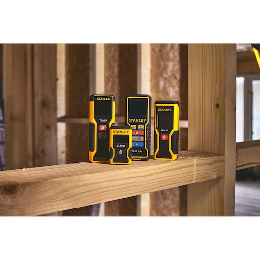 STANLEY STHT1-77343 laser distance meters displayed on wood framing in a construction setting.