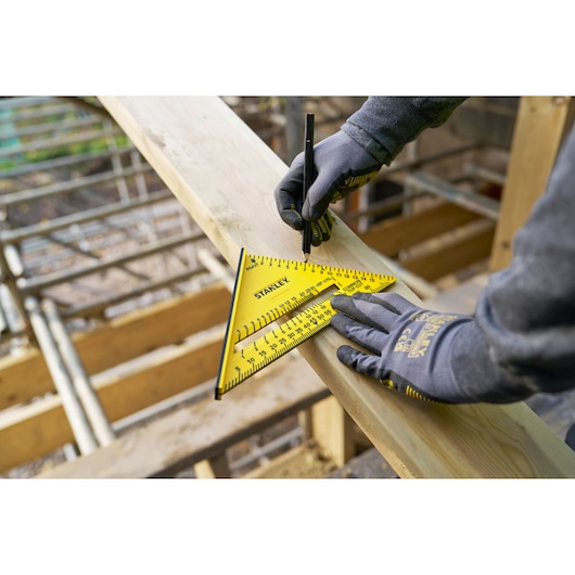 Photo of STANLEY STHT46012-0 yellow rafter square on wood plank, worker marking with pencil, construction site.
