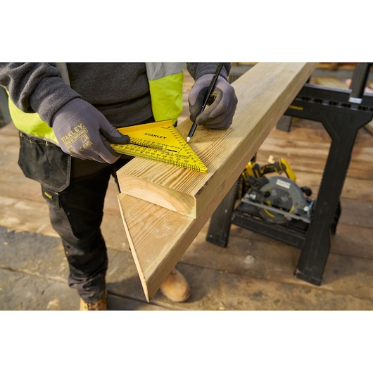 STANLEY STHT46012-0 yellow layout square used to mark wood beam on construction site, close-up angle.