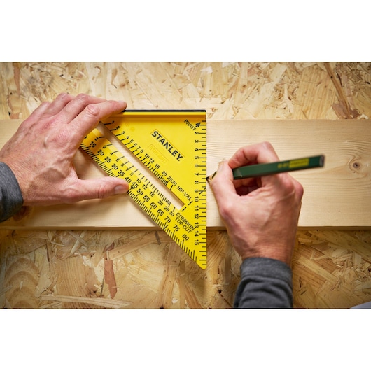 Stanley STHT46012-0 yellow carpenter square used to mark wood on workbench, hands holding pencil and tool.