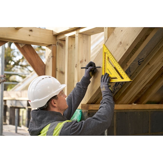 Photo of worker using STANLEY STHT46013-0 yellow rafter square on wooden roof frame, construction site background.