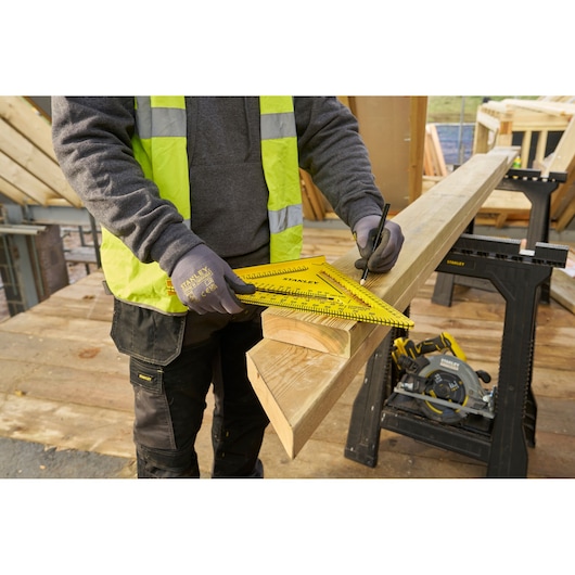 STANLEY STHT46013-0 yellow rafter square used for marking wood on construction site, worker wearing gloves.