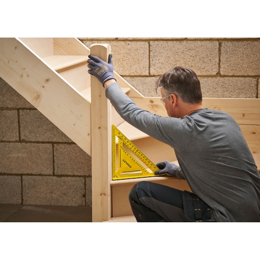 Photo of STANLEY STHT46013-0 yellow plastic rafter square used on wooden staircase by a person wearing gloves.