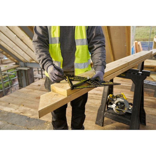 STANLEY STHT46054-0 carpenter using black and yellow framing square to mark wood, construction site background.