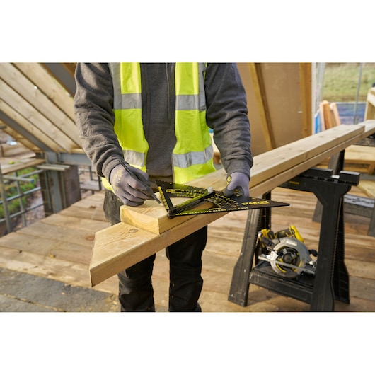 STANLEY STHT46055-0 rafter square in use on wood, construction site background, worker drawing marks.
