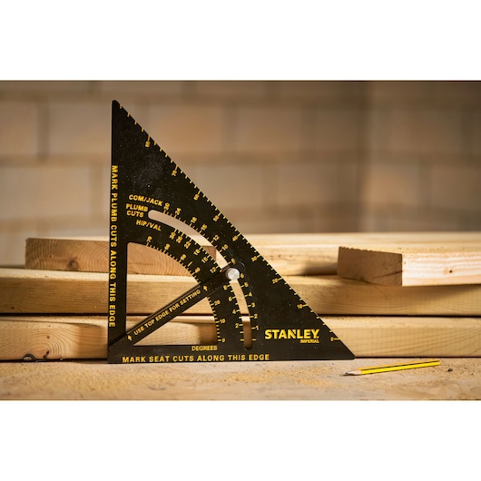 STANLEY STHT46055-0 black and yellow carpenter's square on stacked wood boards with pencil, angled front view.