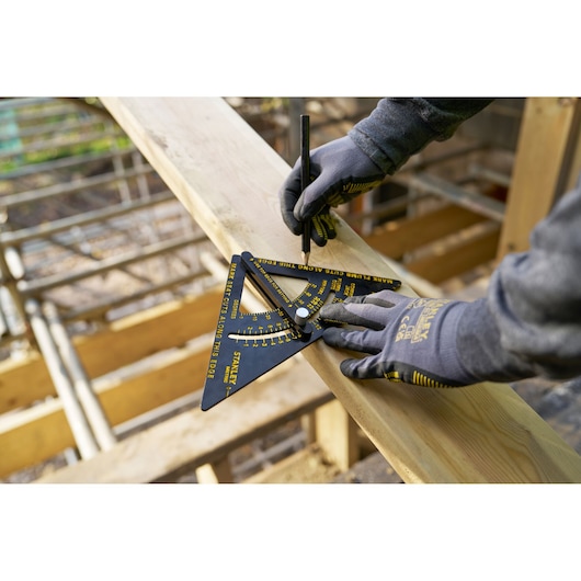 Photo of STANLEY STHT46056-0 carpenter's square tool in use on wooden plank, worker wearing gloves marking wood.