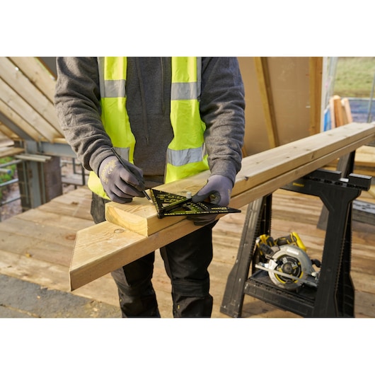 STANLEY STHT46056-0 rafter square on wood beam, angled view, used by worker for precise marking on construction site.