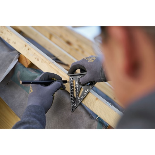Photo of STANLEY STHT46100-0 rafter square in use marking wood, close-up on hands wearing gloves.