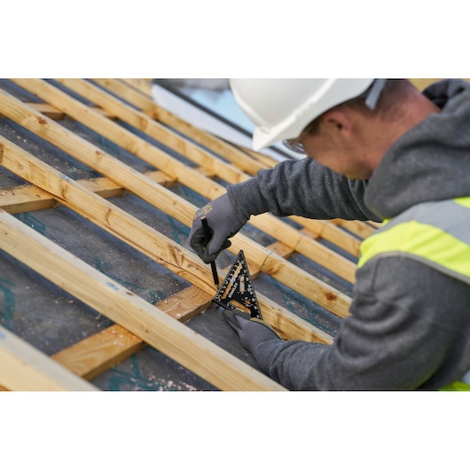 Photo of STANLEY STHT46100-0 black carpenter's square in use on wooden beams, close-up construction scene.