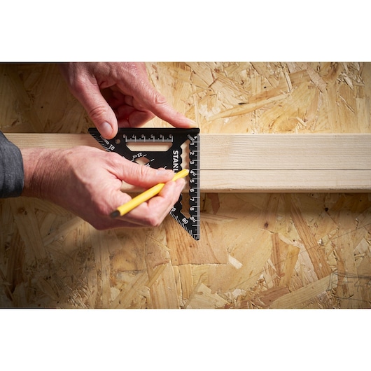 STANLEY STHT46100-0 black carpenter's square in use measuring on wood, hand holding pencil drawing a line.
