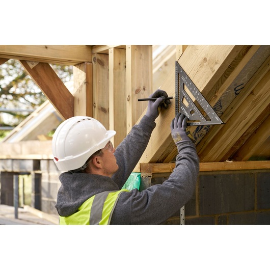 STANLEY STHT46102-0 rafter square used by worker marking wood frame on construction site.
