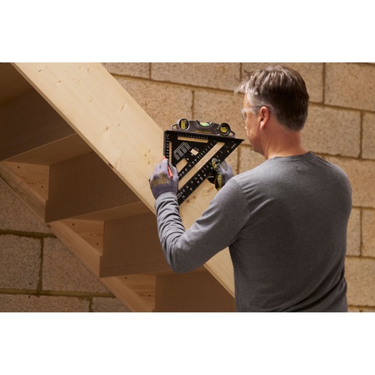 STANLEY STHT46102-0 carpenter using black layout square with level on wooden stairs.