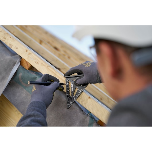 Photo of a person using a STANLEY STHT46103-0 rafter square to mark measurements on a wooden beam during construction.