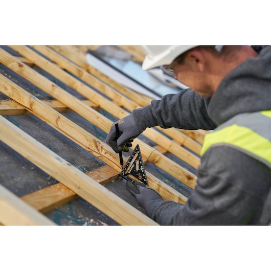 STANLEY STHT46103-0 rafter square in use on wooden roof frame, person marking wood with pencil, outdoor worksite.