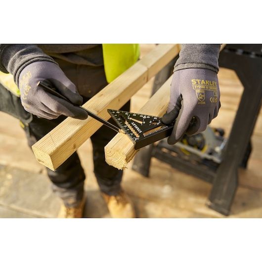 Photo of STANLEY STHT46103-0 layout square marking a wooden beam, gloved hands holding tool and pencil.