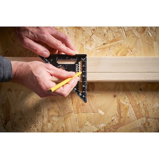 STANLEY STHT46103-0 photography of black speed square being used to mark a wooden board with a pencil.