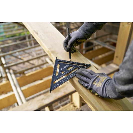 STANLEY STHT46104-0 rafter square used for marking on wood by a gloved hand, construction site background.