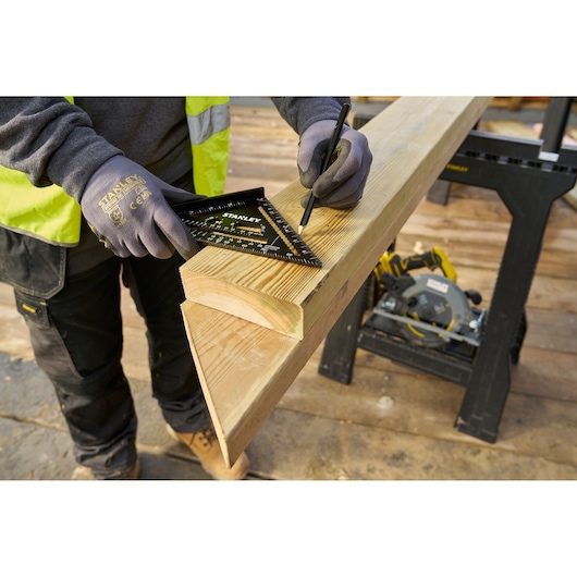 STANLEY STHT46104-0 rafter square used to mark a wooden beam on a jobsite, close-up view.