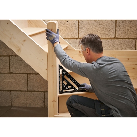 STANLEY STHT46105-0 carpenter using black rafter square on wooden staircase, angled side view.