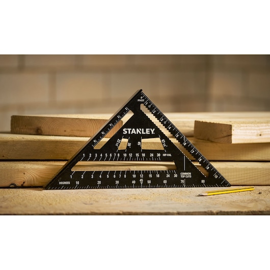 Stanley STHT46105-0 black triangular carpenter's square on wood planks, side angle, with pencil.